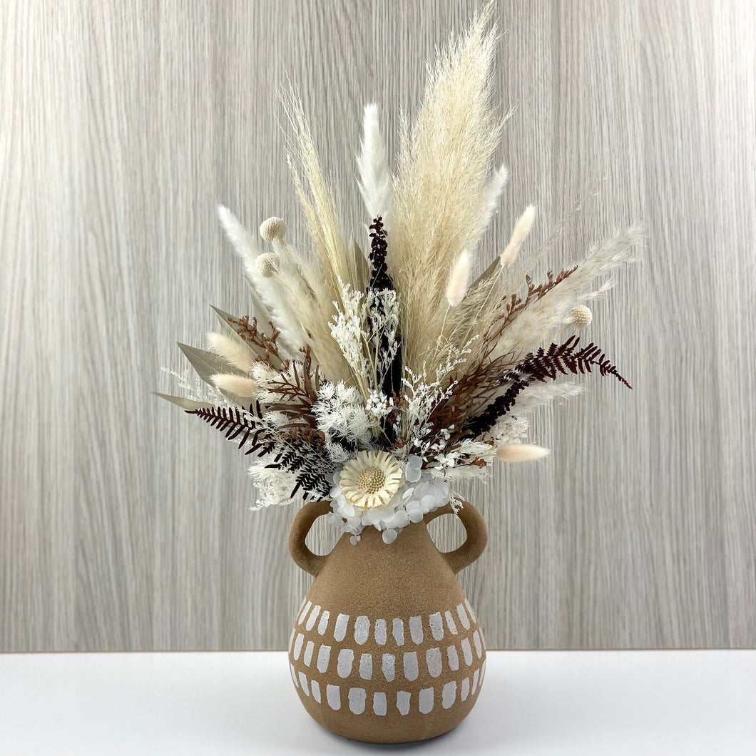 Dried and preserved everlasting arrangement set in a textured handled vase. Flowers consist of pampas, fern, billy buttons, bunny tails, hydrangea, sunflower pod, palm leaf ming fern and other folliage